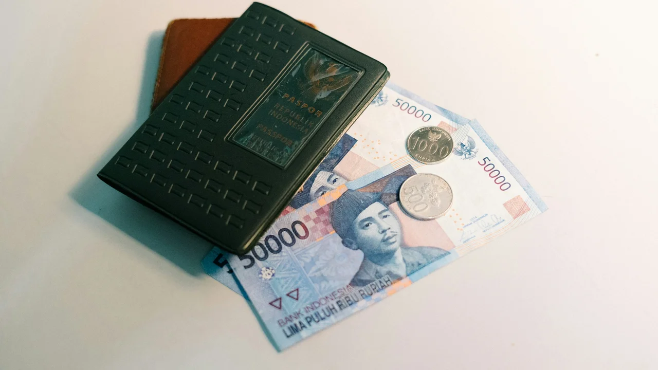 Passport placed on a wallet with Indonesian rupiah banknotes and coins, symbolizing proof of financial means and required funds for a Schengen visa application.