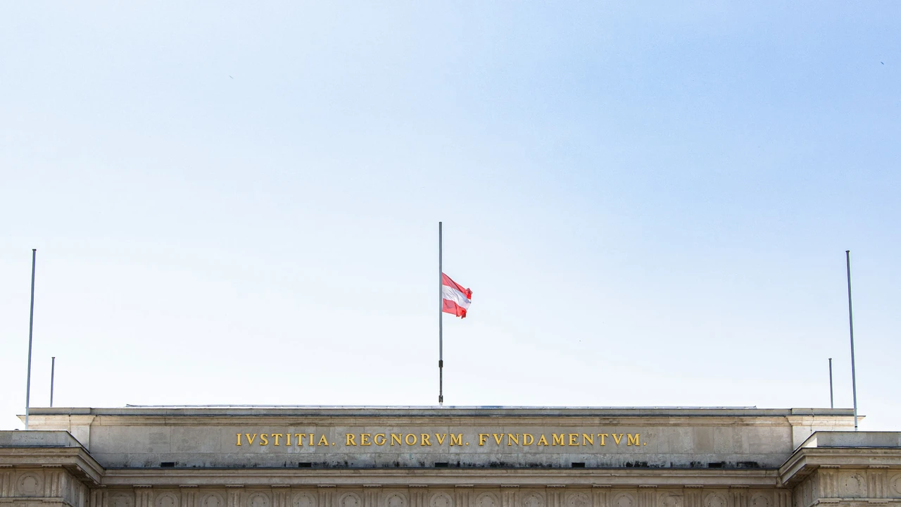 Austria national flag at half mast above historic government building with Latin inscription in Vienna Austria
