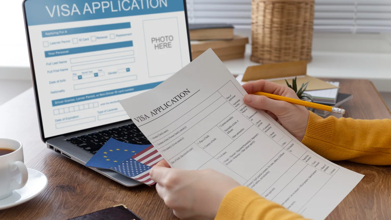 Person filling out a visa application form with US and EU passports on a desk, applying for travel visa online using laptop at home