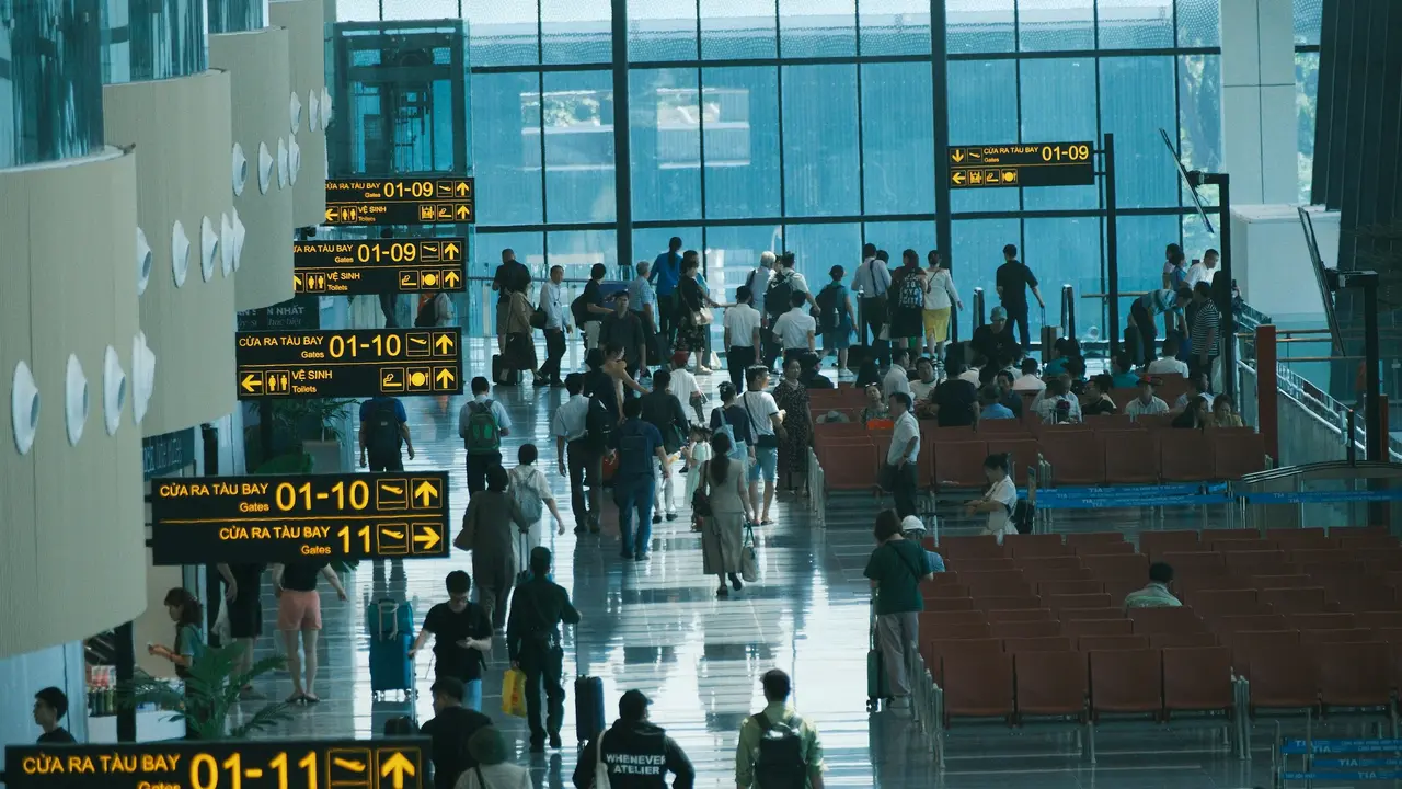 Busy airport departure terminal with travelers walking toward boarding gates and illuminated gate signs in modern international airport