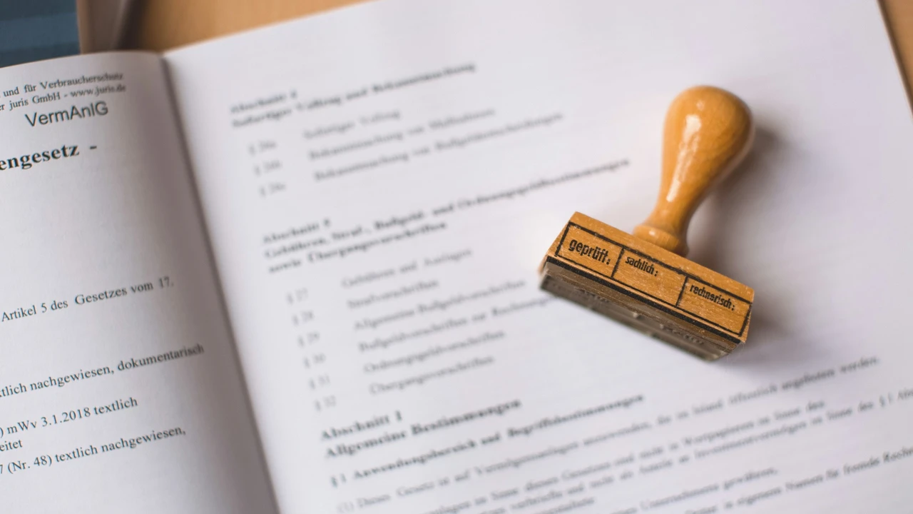 A wooden rubber stamp rests on an open official document containing German text. The stamp has a rectangular base divided into three sections labeled