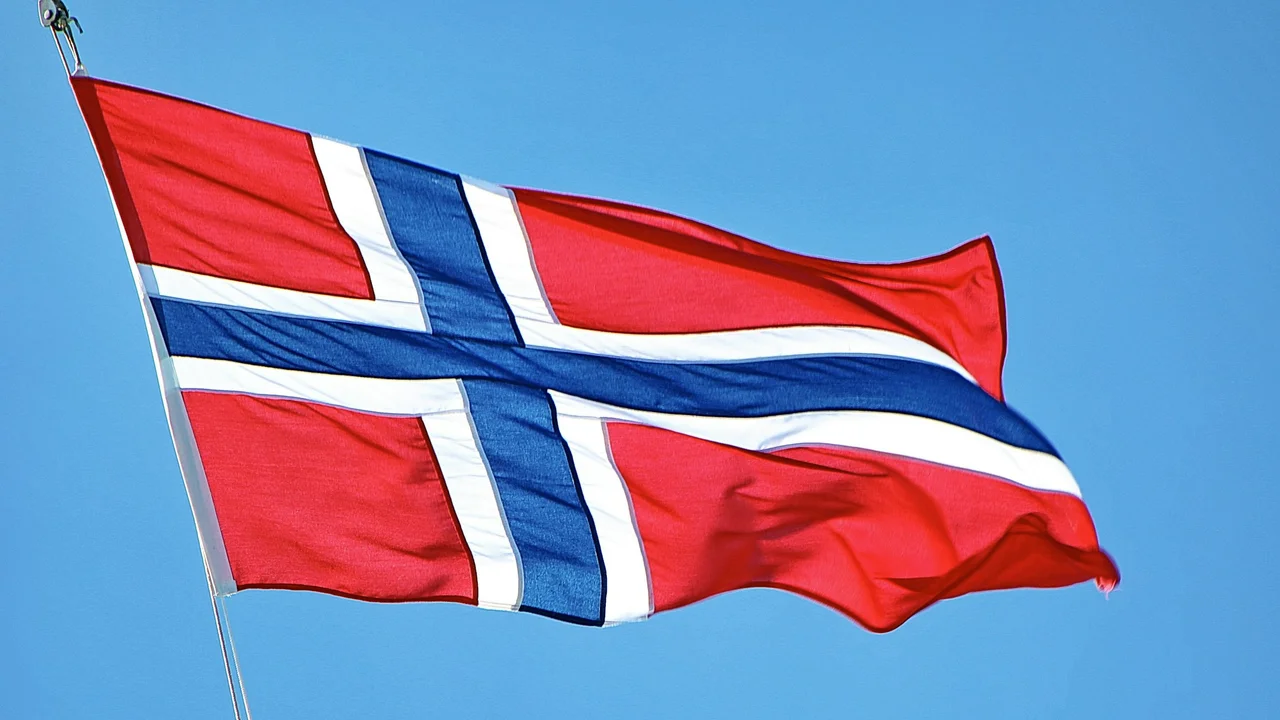 Norwegian national flag waving against a clear blue sky, featuring a red background with a blue Nordic cross outlined in white, symbolizing Norway and Scandinavian heritage.
