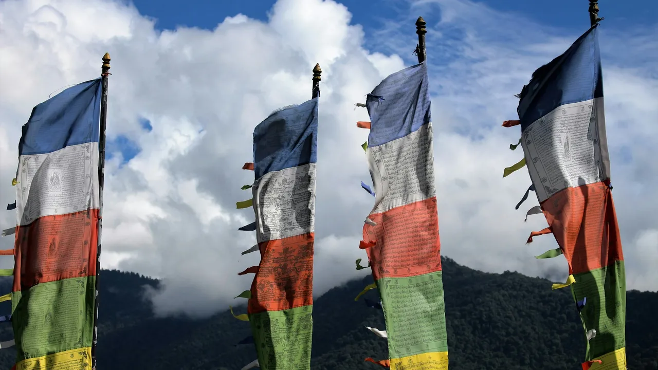 Colorful Bhutanese prayer flags fluttering against Himalayan mountains and cloudy blue sky, symbolizing Bhutan culture and spiritual heritage