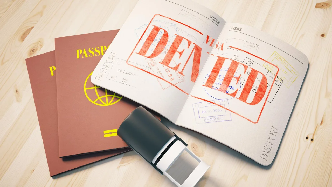 Passport with denied visa stamp and entry stamps, immigration rejection concept with travel documents and visa refusal notice on wooden desk