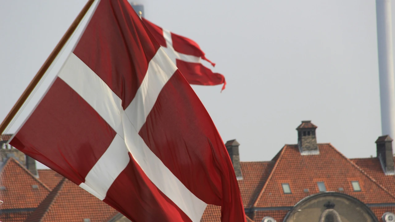 Danish national flag waving in front of historic buildings, representing Denmark visa requirements and information on who needs a visa to travel to Denmark.