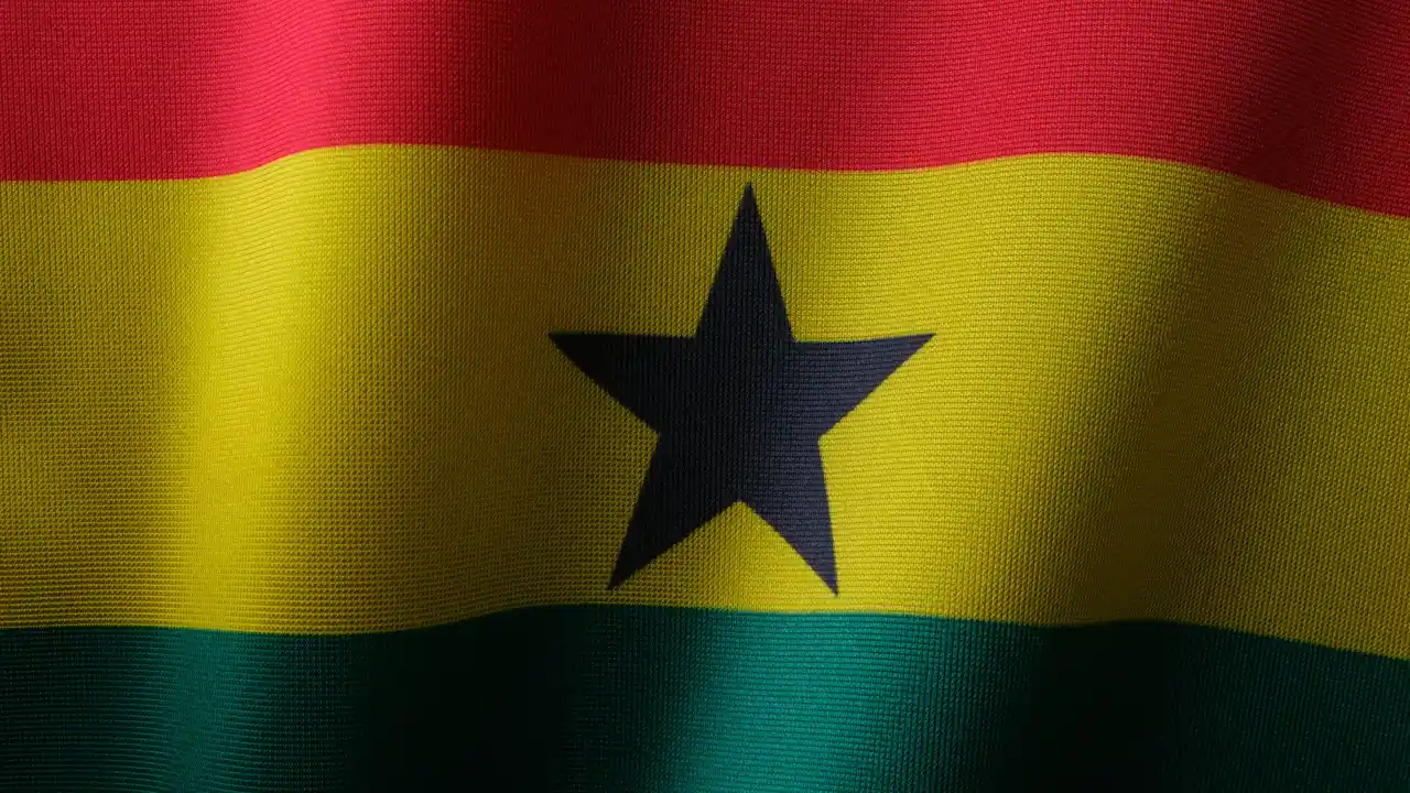 A close-up view of the Ghanaian national flag, featuring its horizontal stripes of red, yellow, and green with a prominent black five-pointed star in the center. The fabric has a visible woven texture and gentle folds, creating a sense of movement.