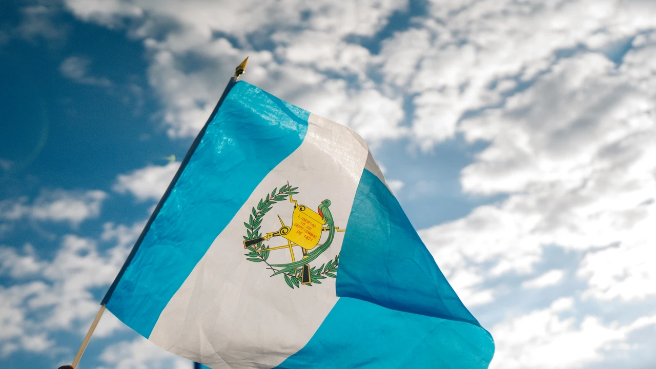 Guatemala national flag waving against a bright blue sky with clouds, symbolizing Guatemala country identity and international travel.