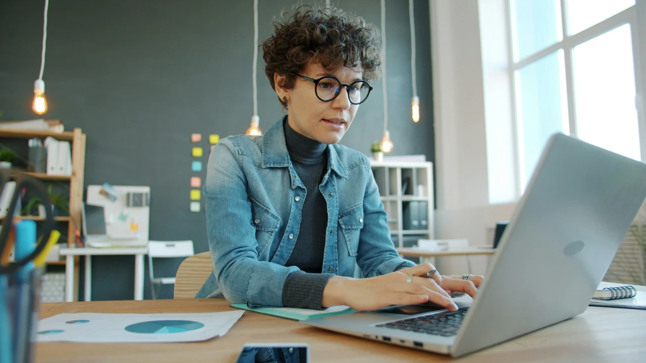Professional woman working on a laptop at a desk in a modern office, reviewing documents and charts, representing online visa application process, paperwork preparation, and how to apply for a Luxembourg visa from Ghana.
