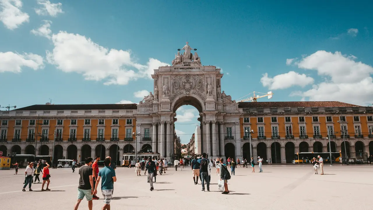 Tourists walking through Praça do Comércio toward the Arco da Rua Augusta in Lisbon Portugal under a bright blue sky