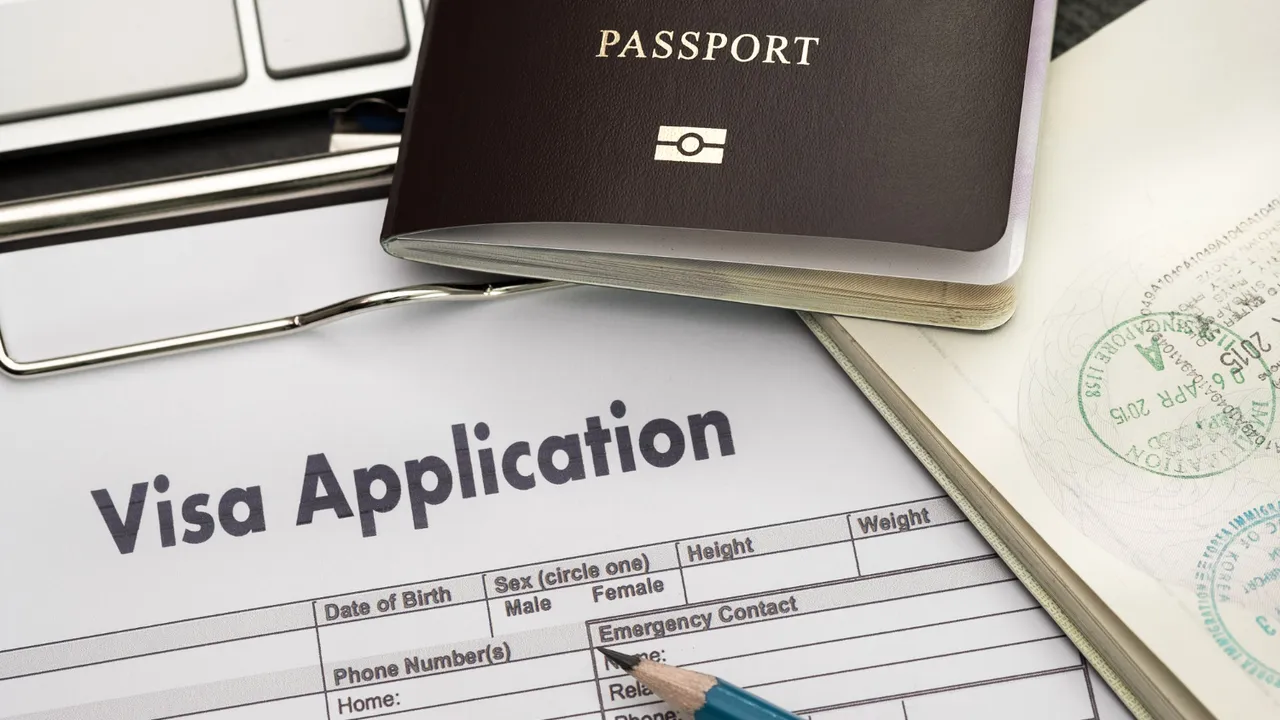 Close-up of visa application form with passport, visa stamp, laptop keyboard, and pen on desk, symbolizing international travel and immigration process