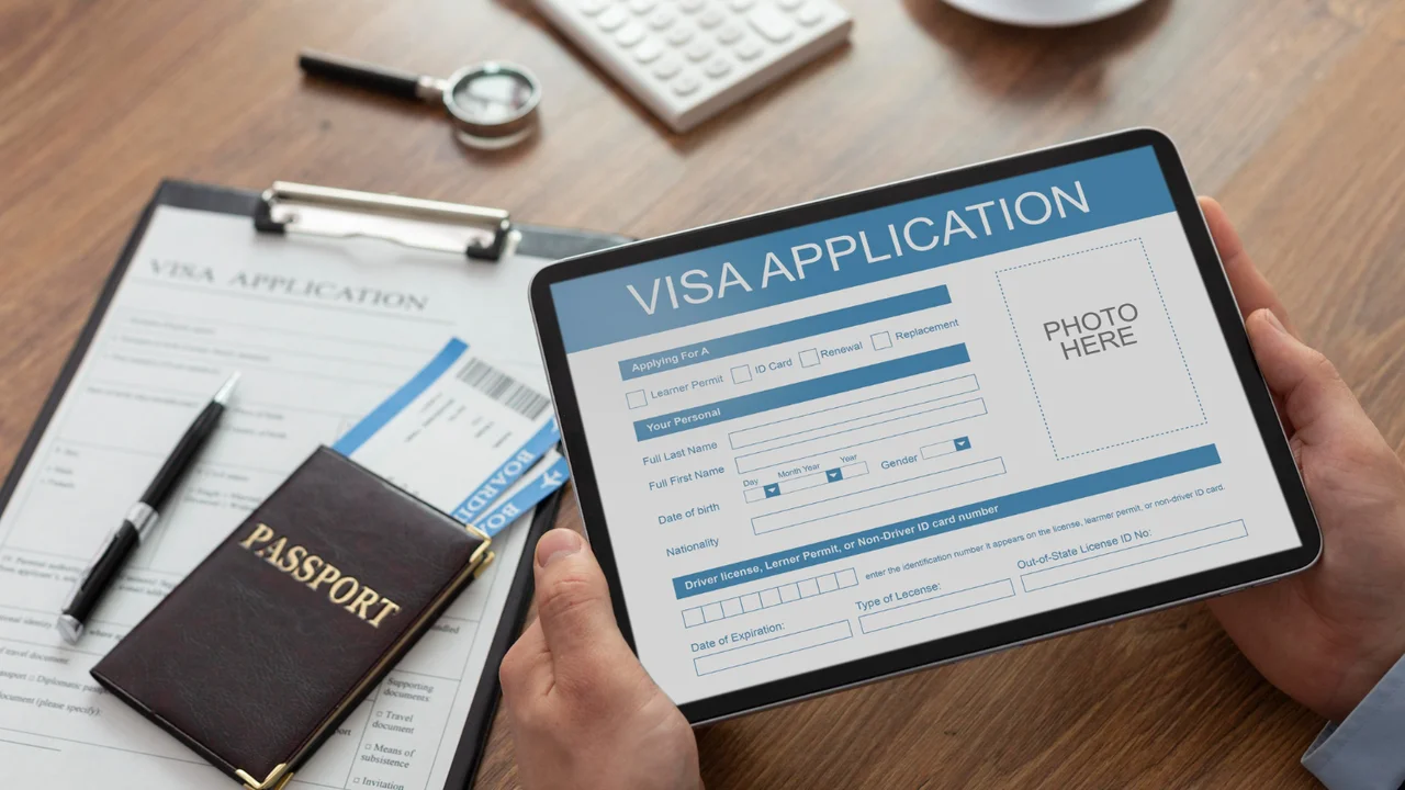Person holding a tablet displaying an online visa application form next to a passport, travel documents, and ID card on a desk, illustrating digital visa processing and international travel documentation.