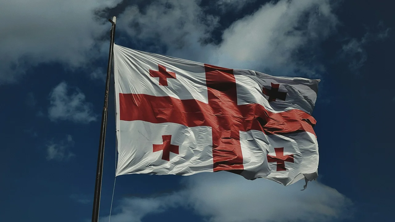 Georgia national flag waving on flagpole against blue sky with clouds, white field with red cross and four smaller crosses
