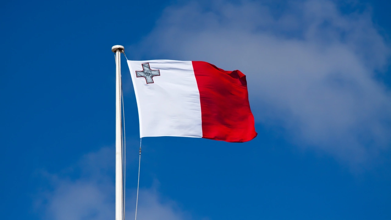 Malta national flag waving on a flagpole against a bright blue sky, featuring the white and red vertical stripes with the George Cross emblem.