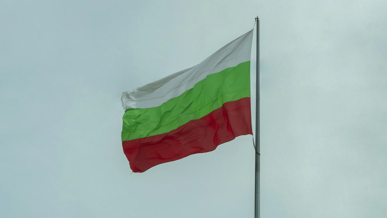 Bulgarian national flag with white, green, and red horizontal stripes flying on a flagpole against a cloudy sky.