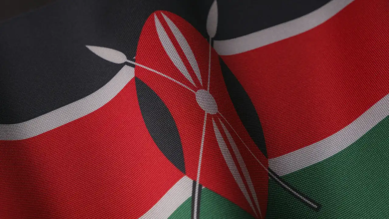 A high-detail, close-up shot of the Kenyan flag's fabric, focusing on the central Maasai shield and crossed spears over the red, black, and green horizontal stripes.