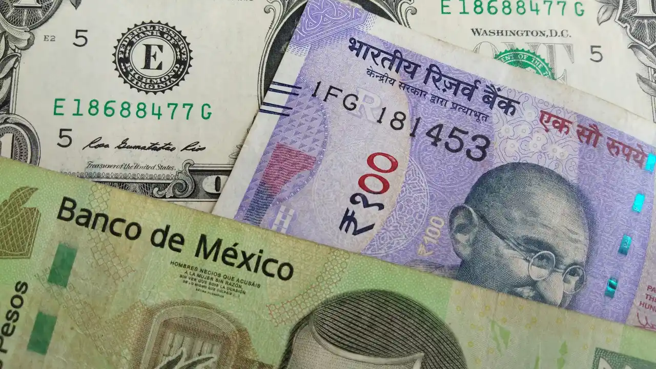 Close-up of international currency notes including a U.S. five-dollar bill, an Indian 200-rupee note featuring Mahatma Gandhi, and a Mexican peso bill from Banco de México, arranged in an overlapping layout.