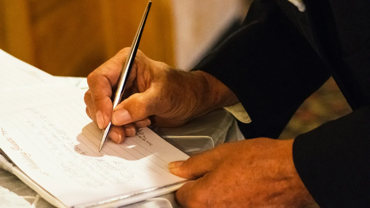 Close-up of a person filling out a visa application form by hand, signing official immigration paperwork with a pen on a document.