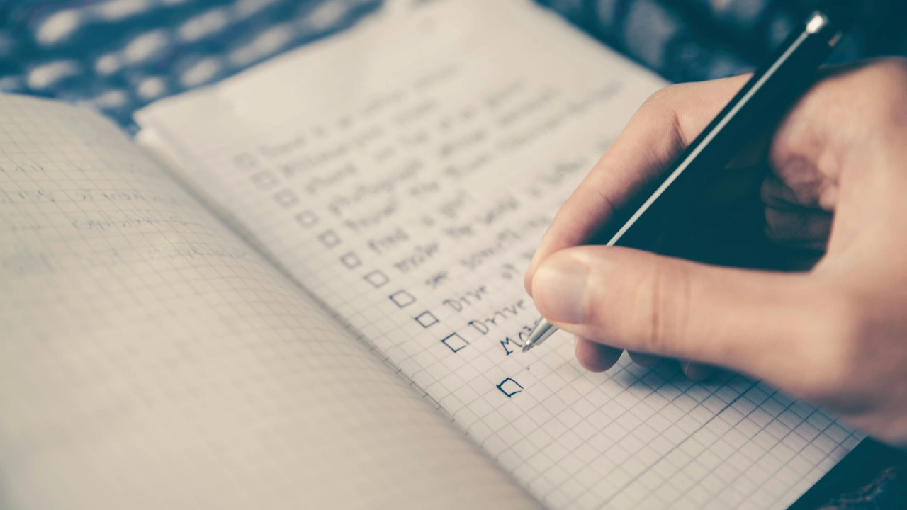 Close up of hand writing checklist in notebook with pen planning daily tasks and goals on grid paper