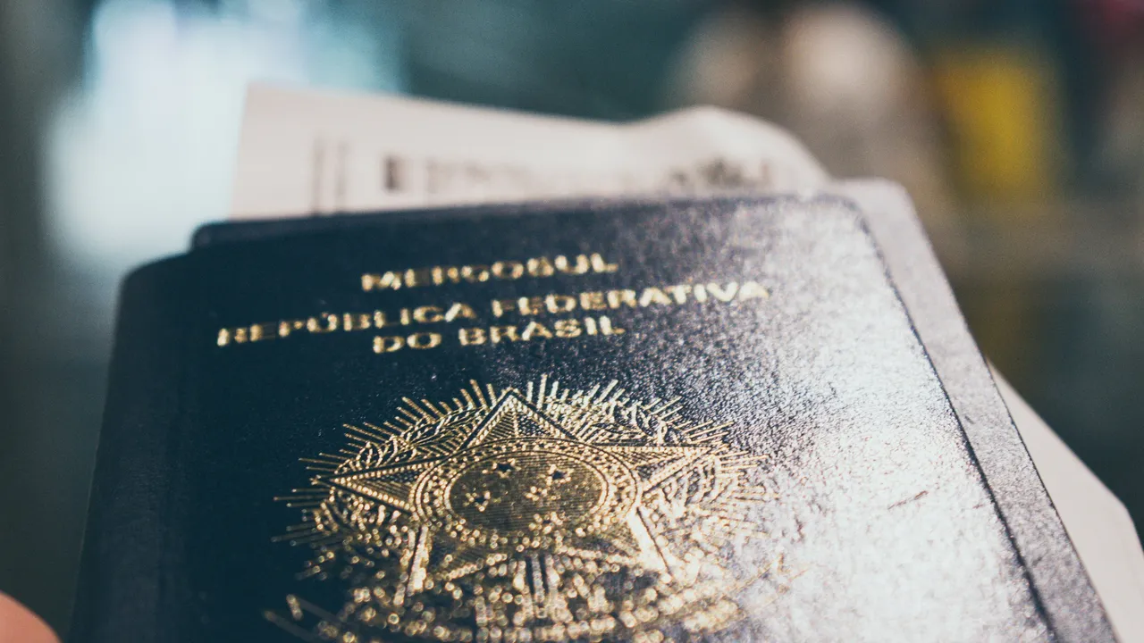 Close-up of a Brazilian passport showing the gold emblem and text “República Federativa do Brasil,” with travel documents partially visible in the background.