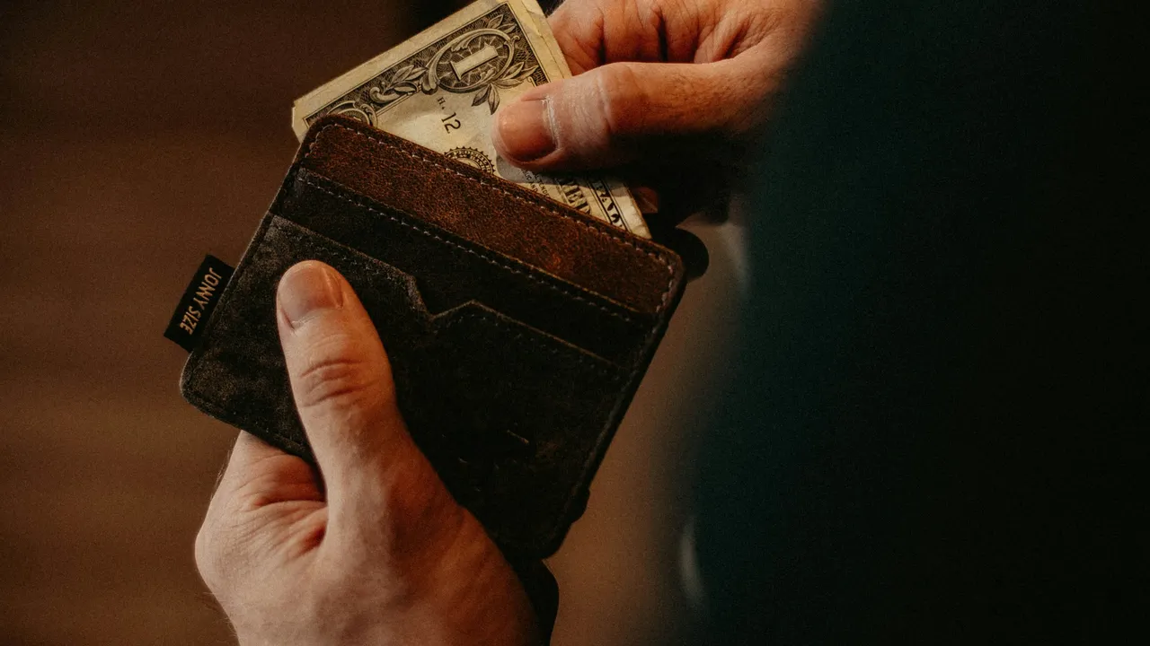 Close-up of a man pulling US dollar cash from a brown leather wallet, personal finance and money management concept