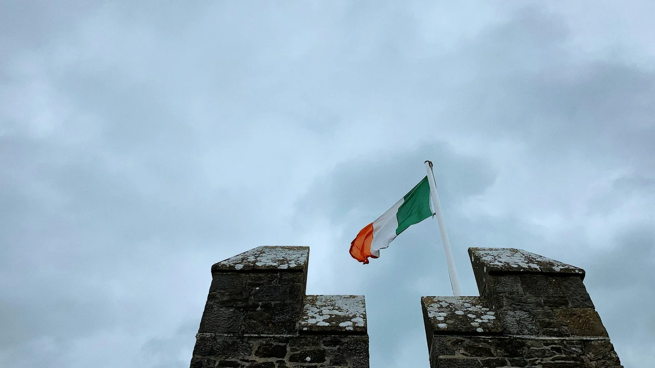 An image of the Irish flag waving against the backdrop of a grand building in Dublin, Ireland. To the left, a white graphic overlay includes the text