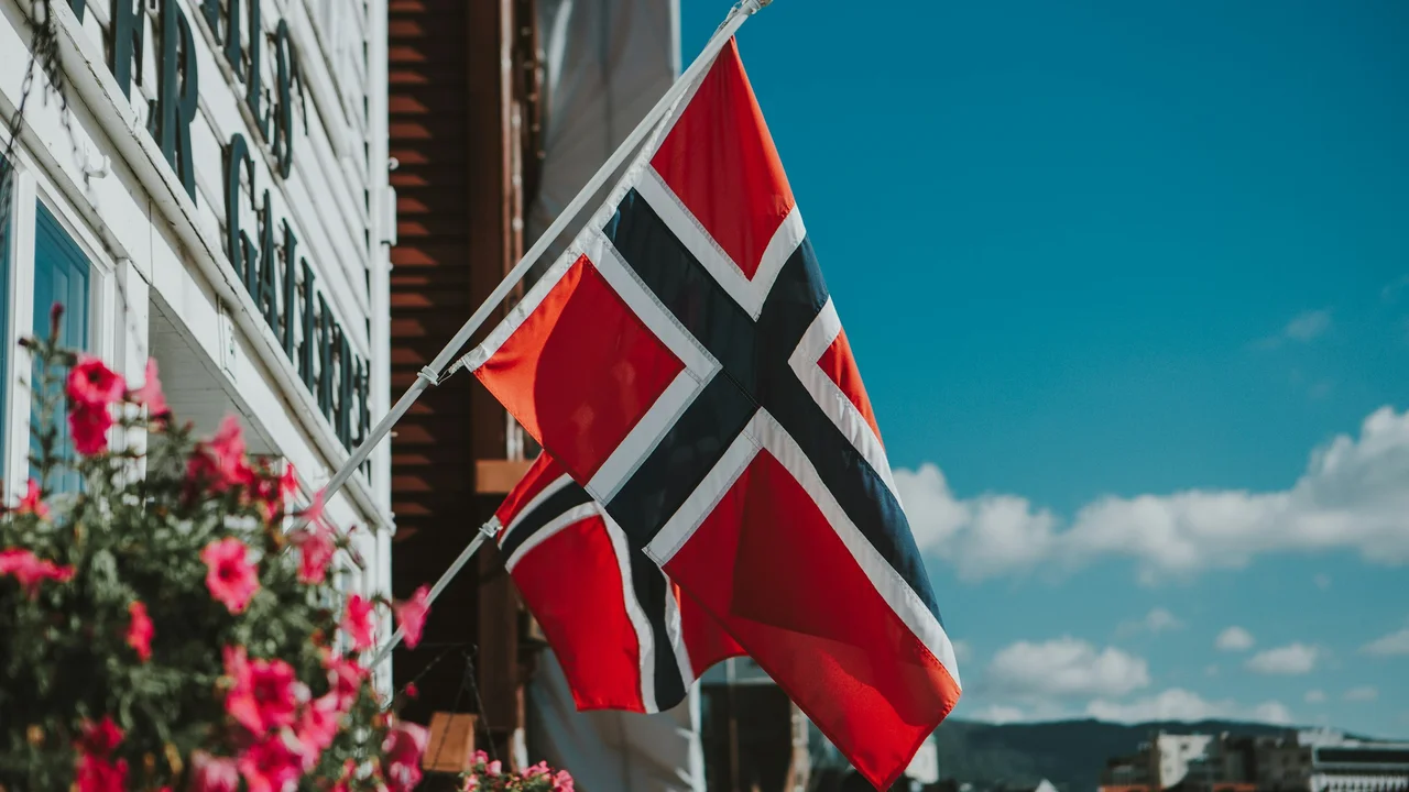 Norwegian flag waving outside building under blue sky – Norway national flag symbol for travel, tourism, and visa information.