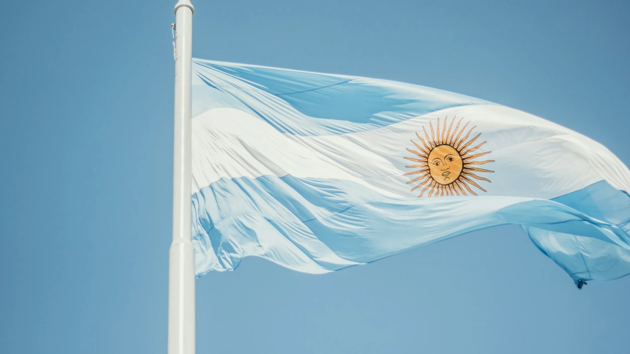 A close-up shot of the national flag of Argentina waving against a clear, bright blue sky. The flag features three horizontal bands of light blue and white, with the golden Sun of May emblem centered in the middle white band.