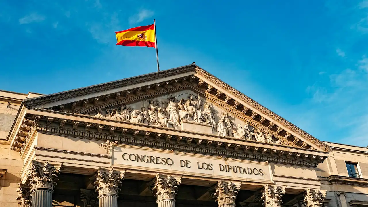Facade of the Congreso de los Diputados in Madrid, Spain, with neoclassical columns, sculpted pediment, and the Spanish flag flying against a blue sky.