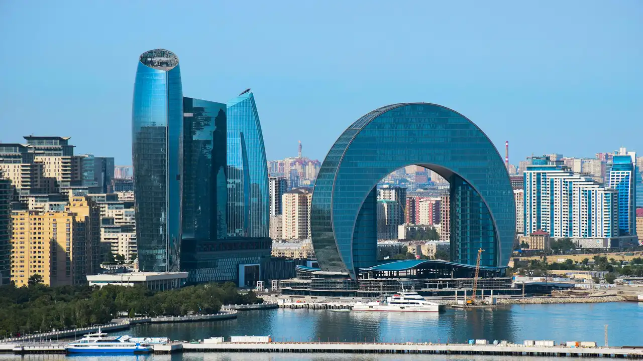 Modern Baku city skyline featuring contemporary glass buildings along the waterfront, including iconic architectural landmarks by the Caspian Sea.