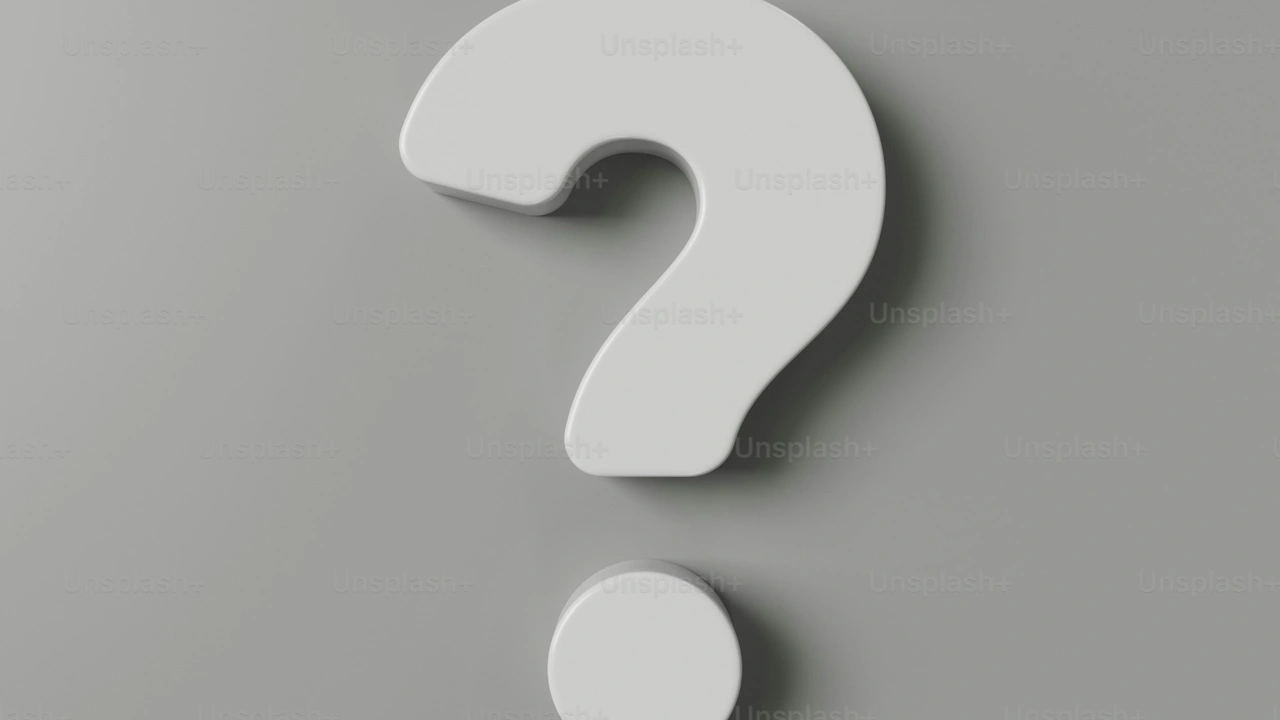A 3D, minimalist white question mark with rounded edges is centered against a flat, neutral gray background. The lighting creates a subtle shadow beneath the symbol, giving it a sense of depth and clean, modern design.